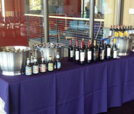 Table with bottles of wine, beer, and buckets of ice, set up for a beverage service at an indoor event.
