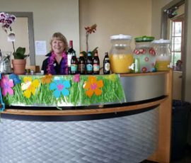 A woman stands behind a decorated drink counter with bottles, jars of juice, and tropical-themed decorations.