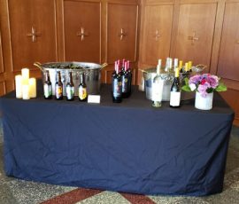 A table with beer bottles, wine bottles, candles, and flowers set up against a wood-paneled wall.