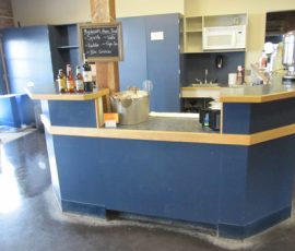 A small blue counter with bottles and a metal ice bucket in a room with kitchen appliances and a chalkboard menu.