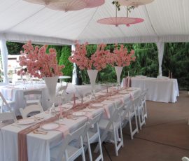 White tent event with pink parasols overhead, pink floral centerpieces, and tables set with pink runners and white chairs.