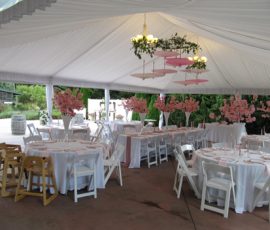 White tented event space with round tables, pink floral centerpieces, and white chairs set for a formal gathering.