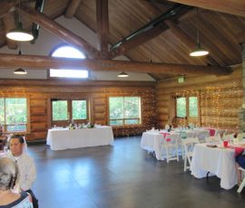 A log cabin event space with decorated tables, string lights on the wall, and a stone fireplace.