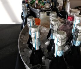 Bottles of wine and liquor are chilled in ice-filled tubs on a table, with more bottles and glasses in the background.