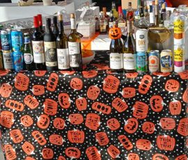 Table covered with a Halloween-themed cloth displaying assorted bottles of alcohol and cans.