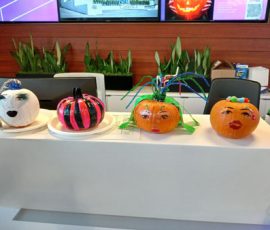 Four decorated pumpkins with painted faces and various embellishments displayed on a table indoors.