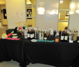 Table set with bottles of wine, ice buckets, cups, and colorful napkins in an indoor setting.