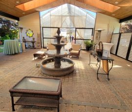 Indoor patio with a central water fountain, wicker furniture, and natural light coming through skylights and open doors.
