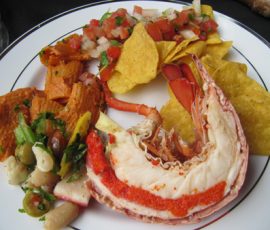 A plate with lobster tail, tortilla chips with salsa, pasta salad, and nacho cheese chips.