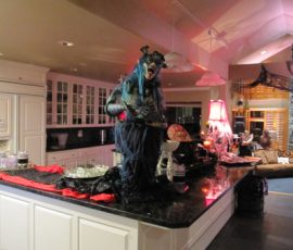 A large monster decoration sits on a kitchen island surrounded by Halloween-themed props and dim lighting.