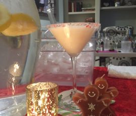 A frosted martini glass, gingerbread man candles, and a lit votive sit on a red tablecloth with ice water in the background.