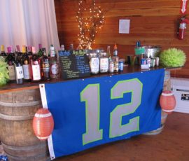 Bar setup with bottles, a drink menu, football lanterns, and a large blue flag with the number 12 draped in front.