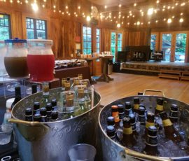 Metal tubs filled with ice and bottled drinks at a beverage station in a rustic wooden event hall with string lights.
