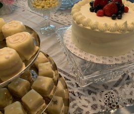 A table with assorted desserts, including petit fours, a berry-topped cake, cookies, and candy on lace tablecloth.