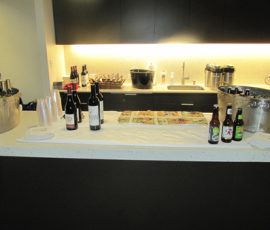 A countertop with wine, beer, soft drinks, cups, napkins, and a tray of snacks set up for a gathering or event.